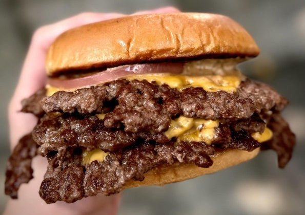 Hand holding a large cheeseburger with multiple beef patties against a blurred background