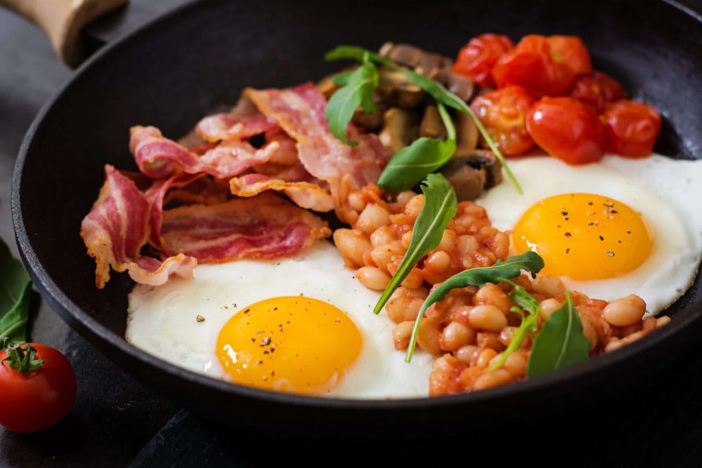 Fried eggs, turkey bacon, beans, and tomatoes in a pan 